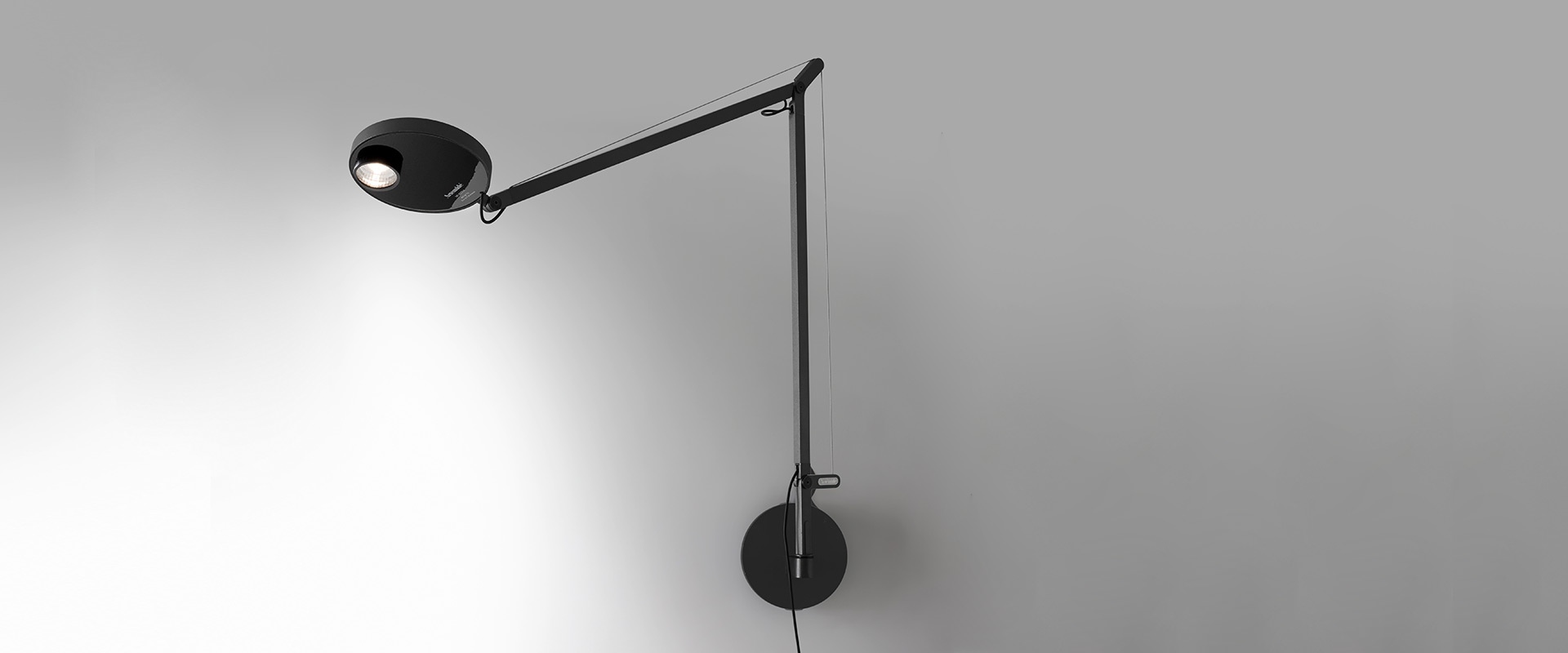 Lampada da parete Artemide Demetra in nero, con braccio regolabile, testa circolare con luce LED e base tonda a parete.