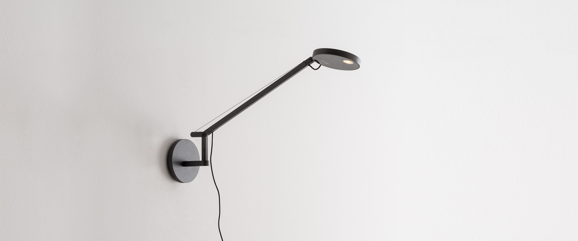 Artemide Demetra Micro wall lamp in anthracite, featuring a slim adjustable arm with circular LED head mounted on a round wall base