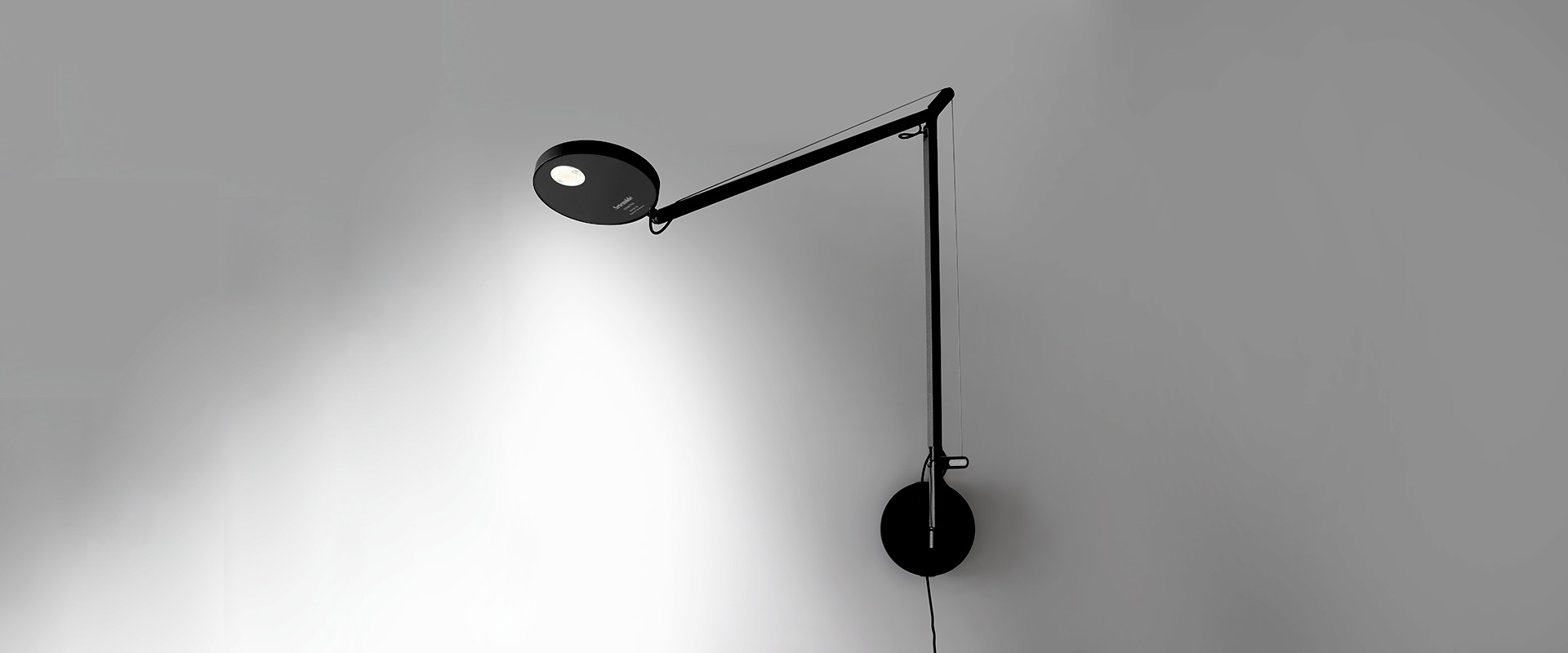 Artemide Demetra Parete wall lamp: white articulated arm with black circular LED head, mounted on wall bracket, casting focused light