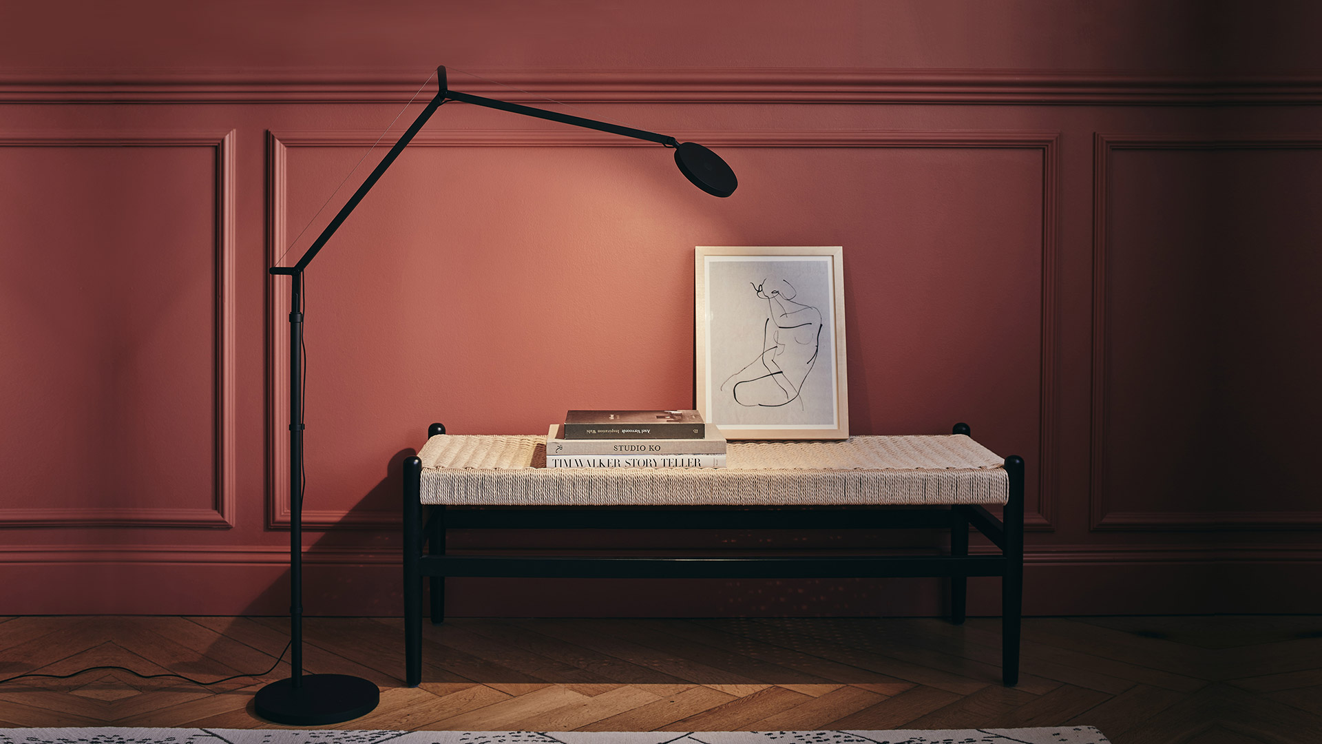 Lampada da terra Artemide Demetra Reading Floor in nero opaco accanto a una panca intrecciata con libri e opera incorniciata su parete rosa