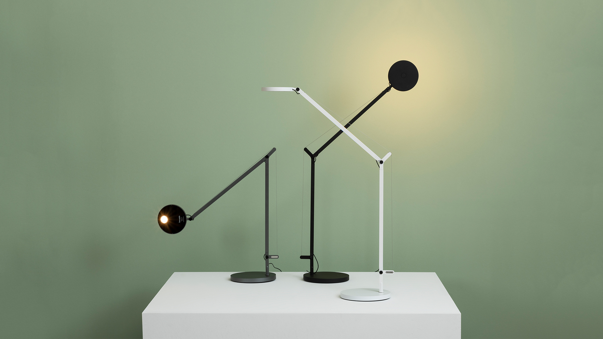 Tre lampade da terra Artemide Demetra con paralumi sferici su sottili steli neri e bianchi, su sfondo verde salvia