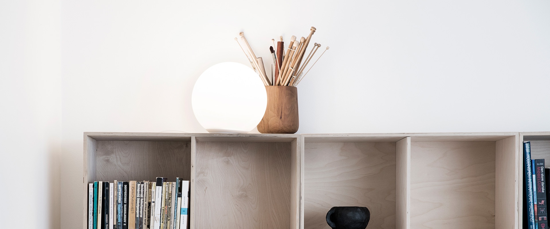 Lampada da tavolo Artemide Dioscuri con diffusore sferico bianco opale su uno scaffale in legno accanto a un porta matite e libri