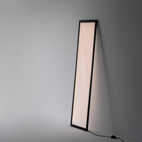 Lampada da terra Artemide Discovery Terra: alto pannello luminoso rettangolare con cornice nera, appoggiato alla parete, emette luce diffusa calda