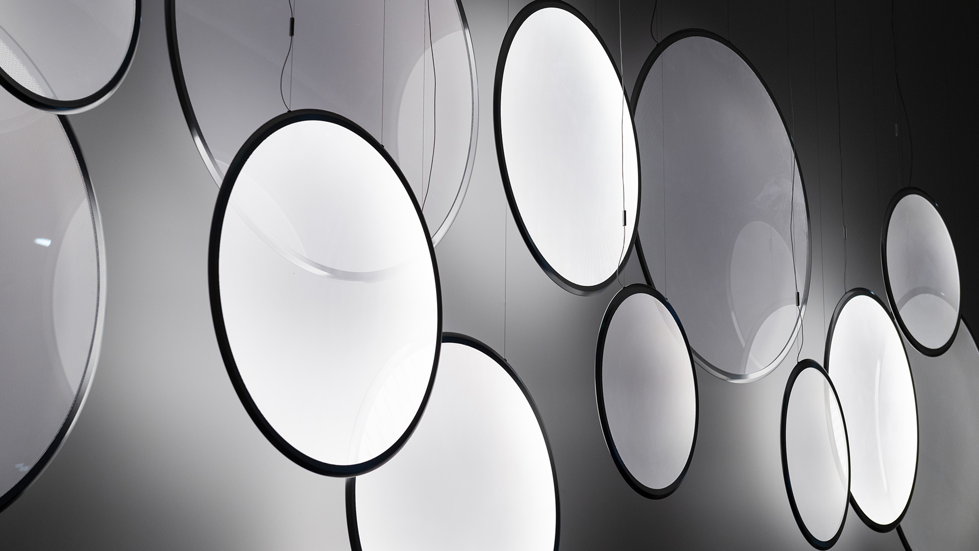 Lampade a sospensione Artemide Discovery con diffusori circolari in luce calda, esposte in una stanza rosa vivace con tavolo e sedia bianchi