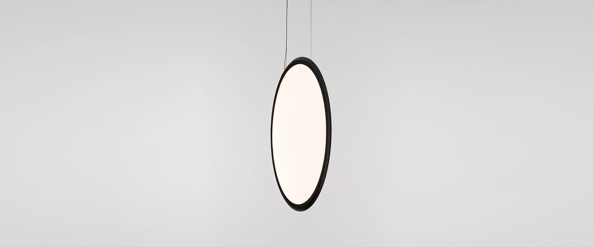 Sala da pranzo elegante con una grande lampada a sospensione circolare Artemide Discovery come punto focale luminoso sopra un tavolo in legno rustico.