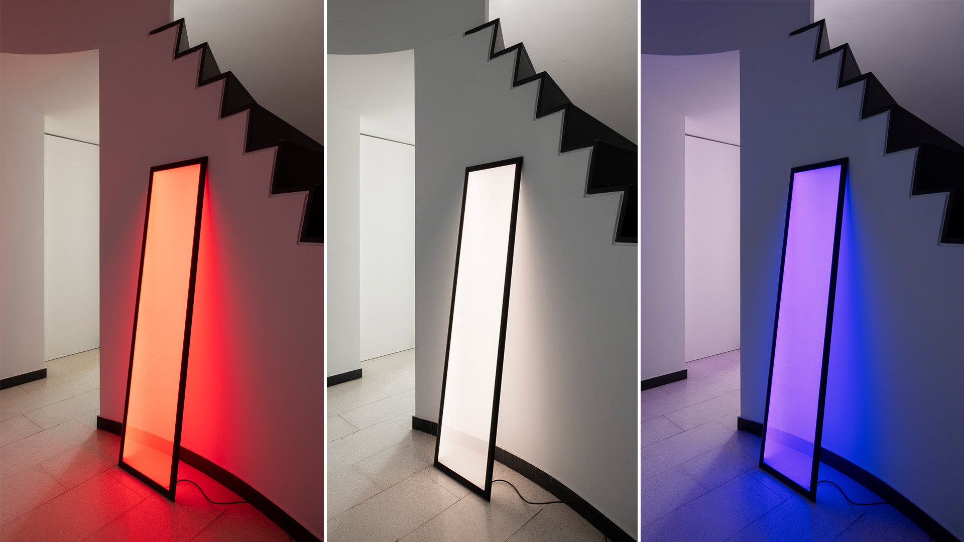 Lampada da terra Artemide Discovery Terra: alto pannello LED rettangolare con cornice nera, appoggiato alla parete, emette luce diffusa calda