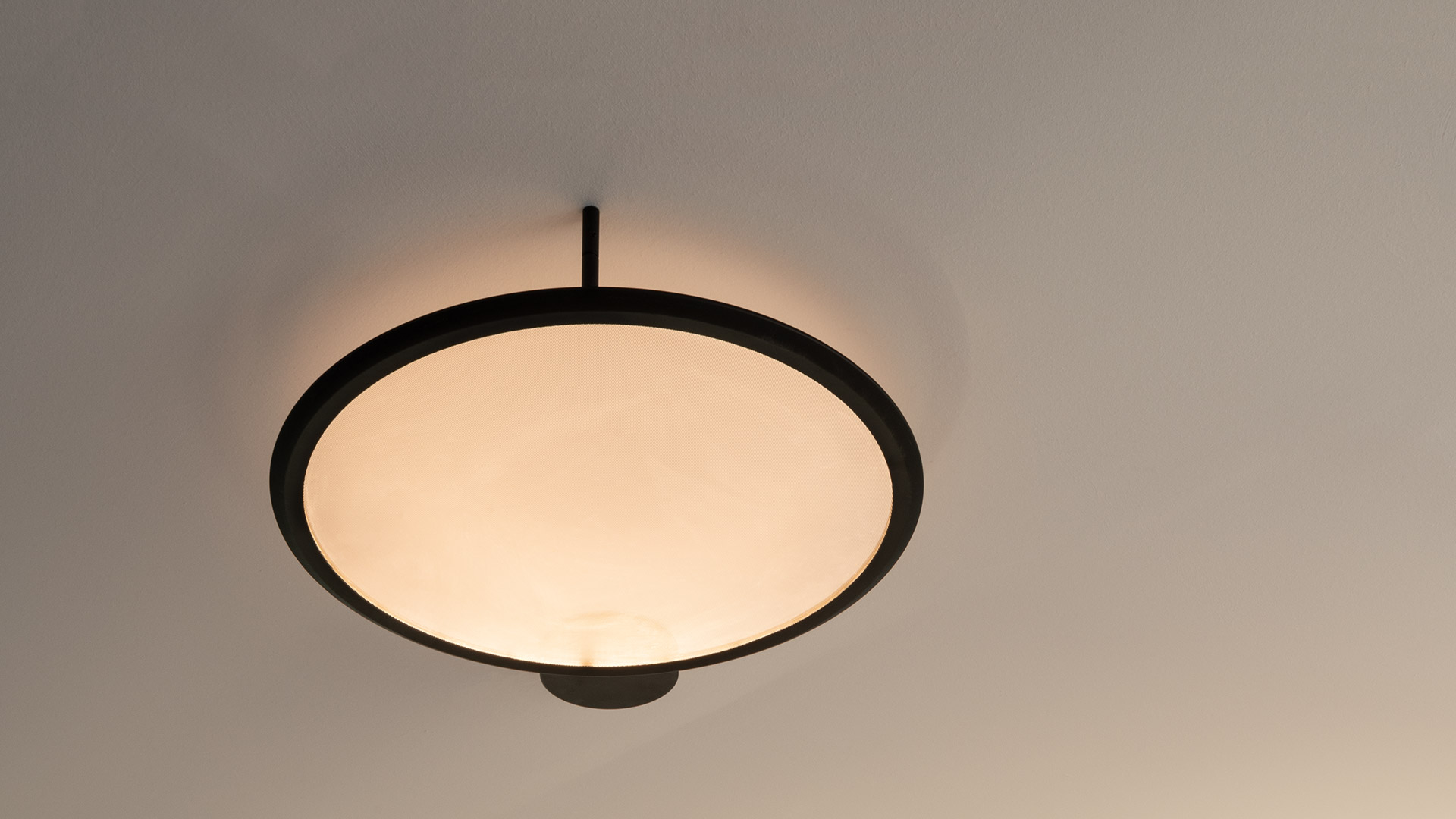 Artemide Discovery Parete wall lamp: large circular white diffuser with dark metal ring emitting soft backlight, small sphere at base