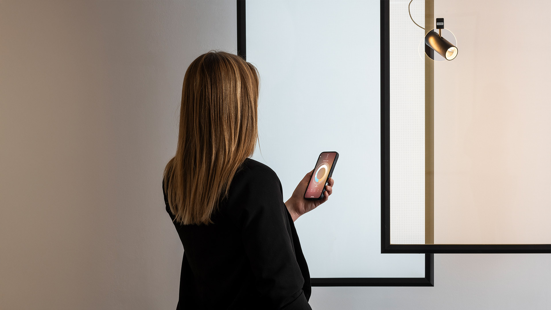 Artemide Discovery Spot: faretto a sospensione nero con testa cilindrica all'interno di un sottile anello circolare, sospeso da un cavo davanti a un pannello a rete