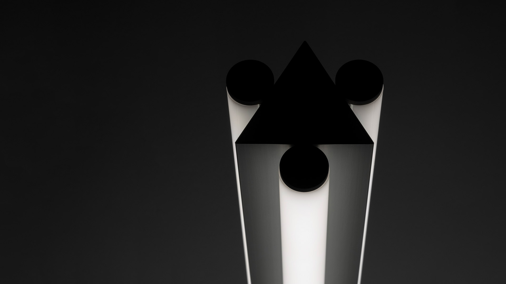 Artemide Dreispitz floor lamp: white luminous triangular column with black geometric shapes—triangle, circles—on dark background