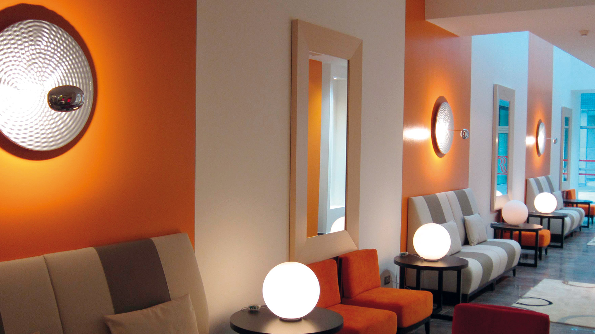 Hotel lounge with orange walls featuring Artemide Droplet wall lights and Droplet Mini white globe table lamps on low black tables