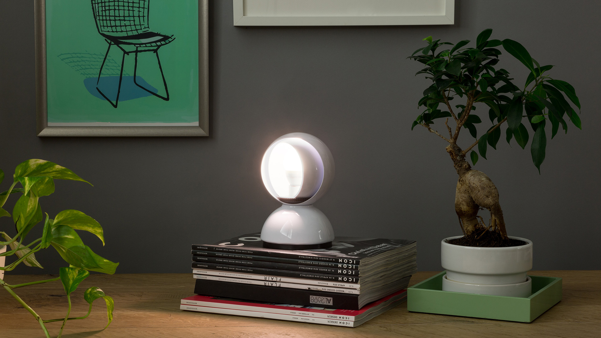 Four Artemide Eclisse table lamps in a row: red, orange, yellow, and white, each with a rotatable inner shell revealing warm light