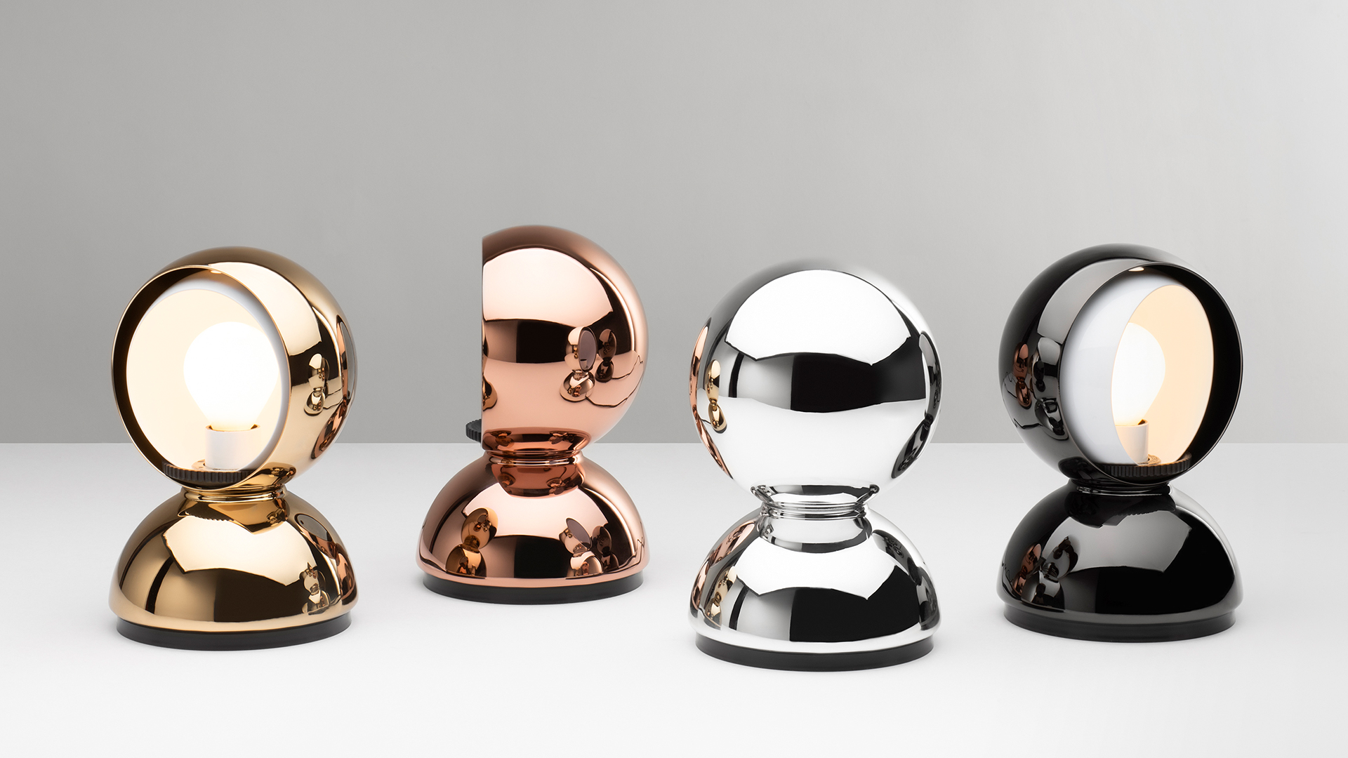 Three Artemide Eclisse table lamps in red, orange, and white, each featuring a rotating spherical shade on a dome-shaped base