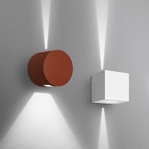 Two Artemide Effetto wall lights: cylindrical rust-red and cubic white, both projecting upward and downward light beams on a grey wall