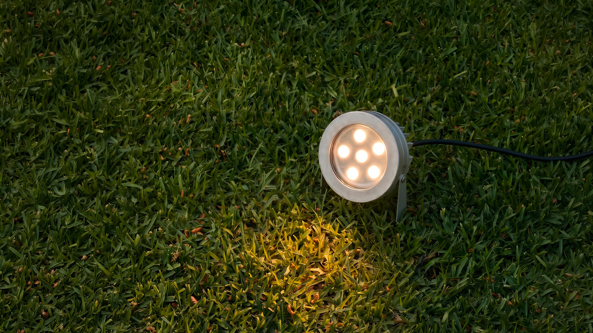 Passaggio coperto esterno di notte con travi in legno illuminate da faretti da incasso Artemide Ego Spot, muro con graffiti a sinistra