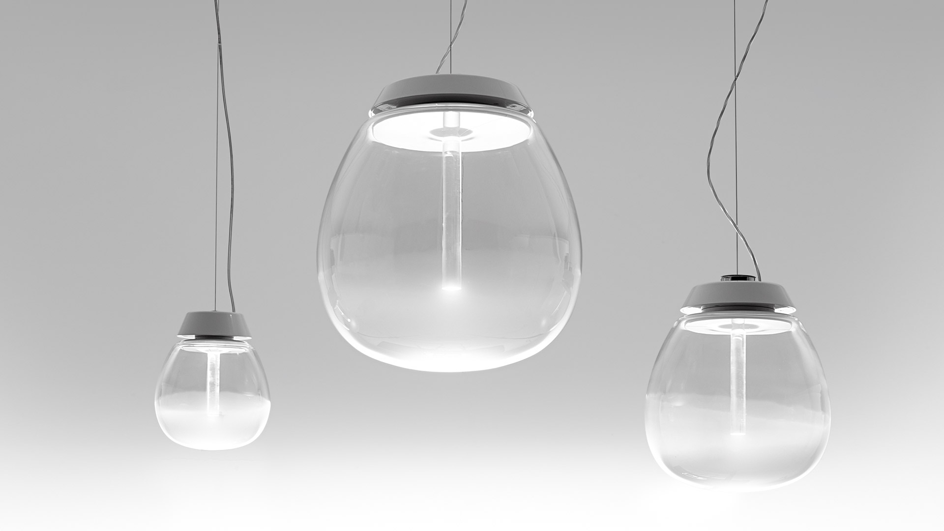 Three Artemide Empatia pendant lamps in different sizes, featuring clear glass globes with grey metal tops, suspended by black cords