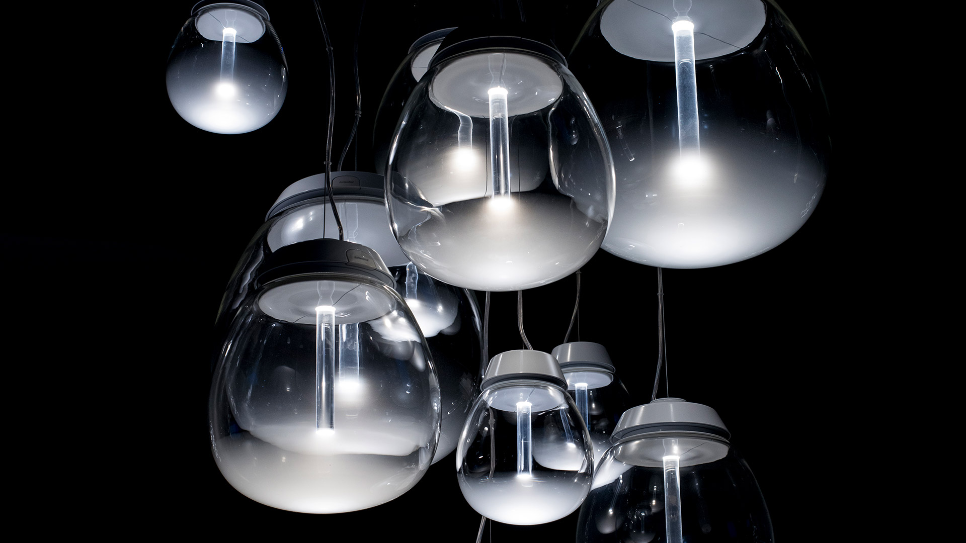 Artemide Empatia pendant lamps: cluster of transparent glass globe shades with integrated LED light sources, suspended against black background