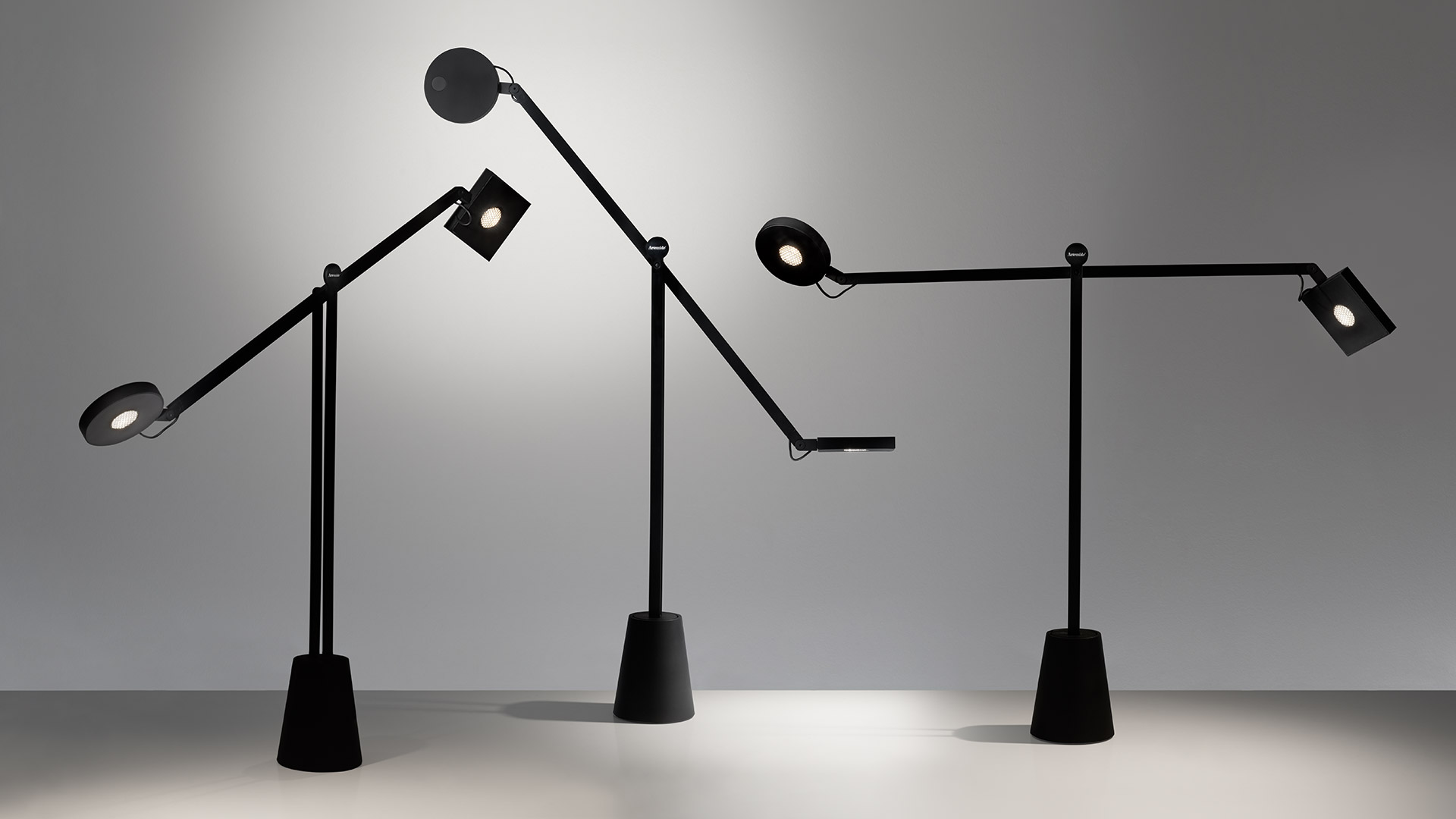 Two Artemide Equilibrist black table lamps with articulated arms and circular heads balanced on conical bases, casting focused light