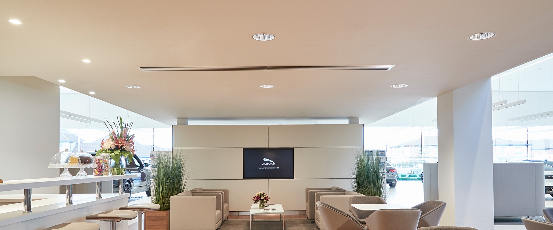 Jaguar dealership lounge with Artemide Everything 150 Trim recessed ceiling lights illuminating a modern seating area with TV screen
