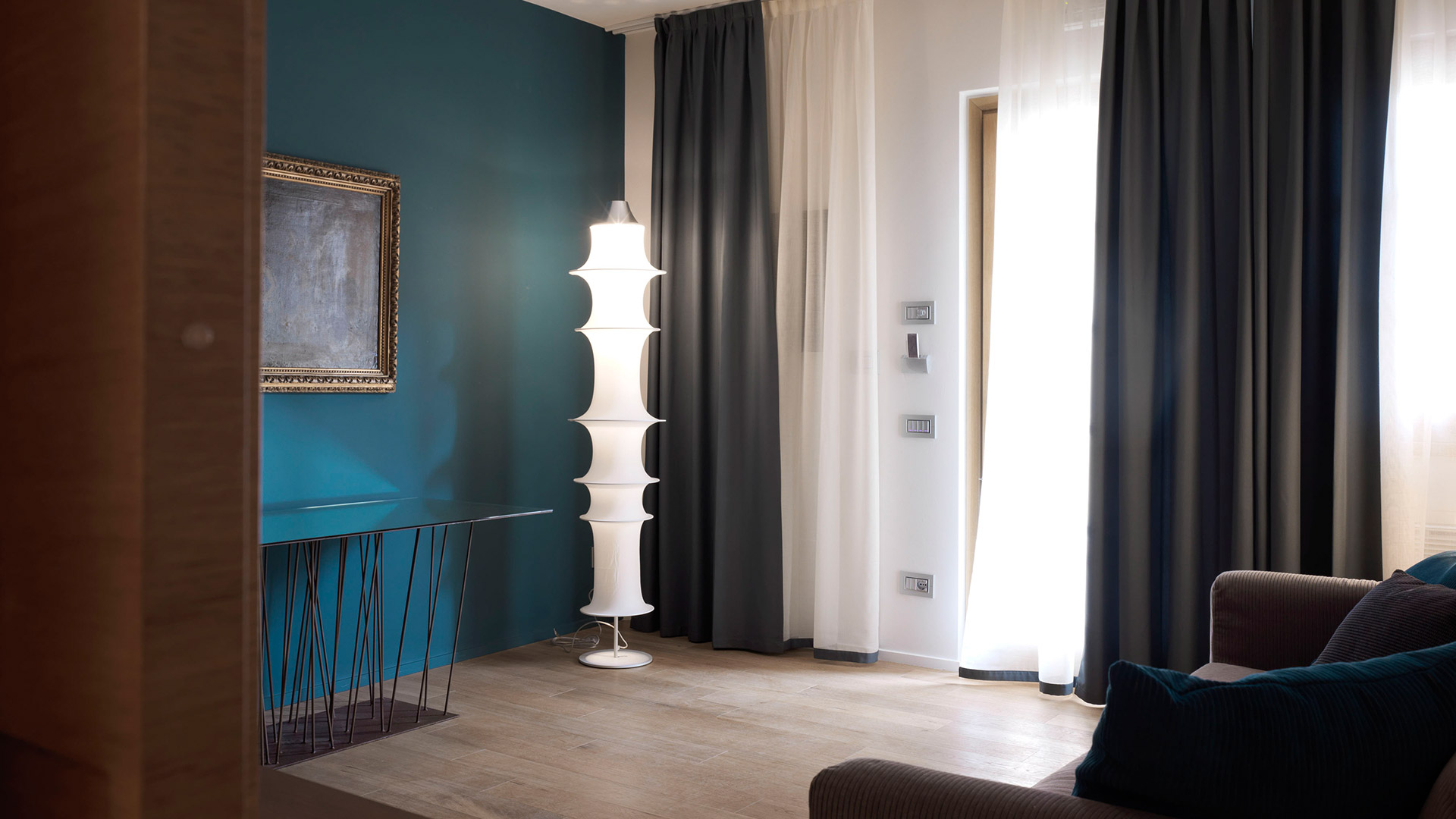 Lampada da terra Artemide Falkland Terra con diffusori ovali sovrapposti in un soggiorno moderno con parete color ottanio e tende grigie