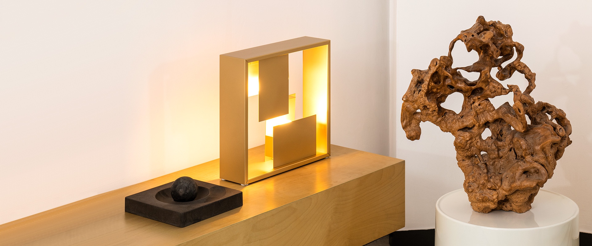 Illuminated display box with glowing white cubic lamp, small sculpture, decorative vase with branches, on dark background