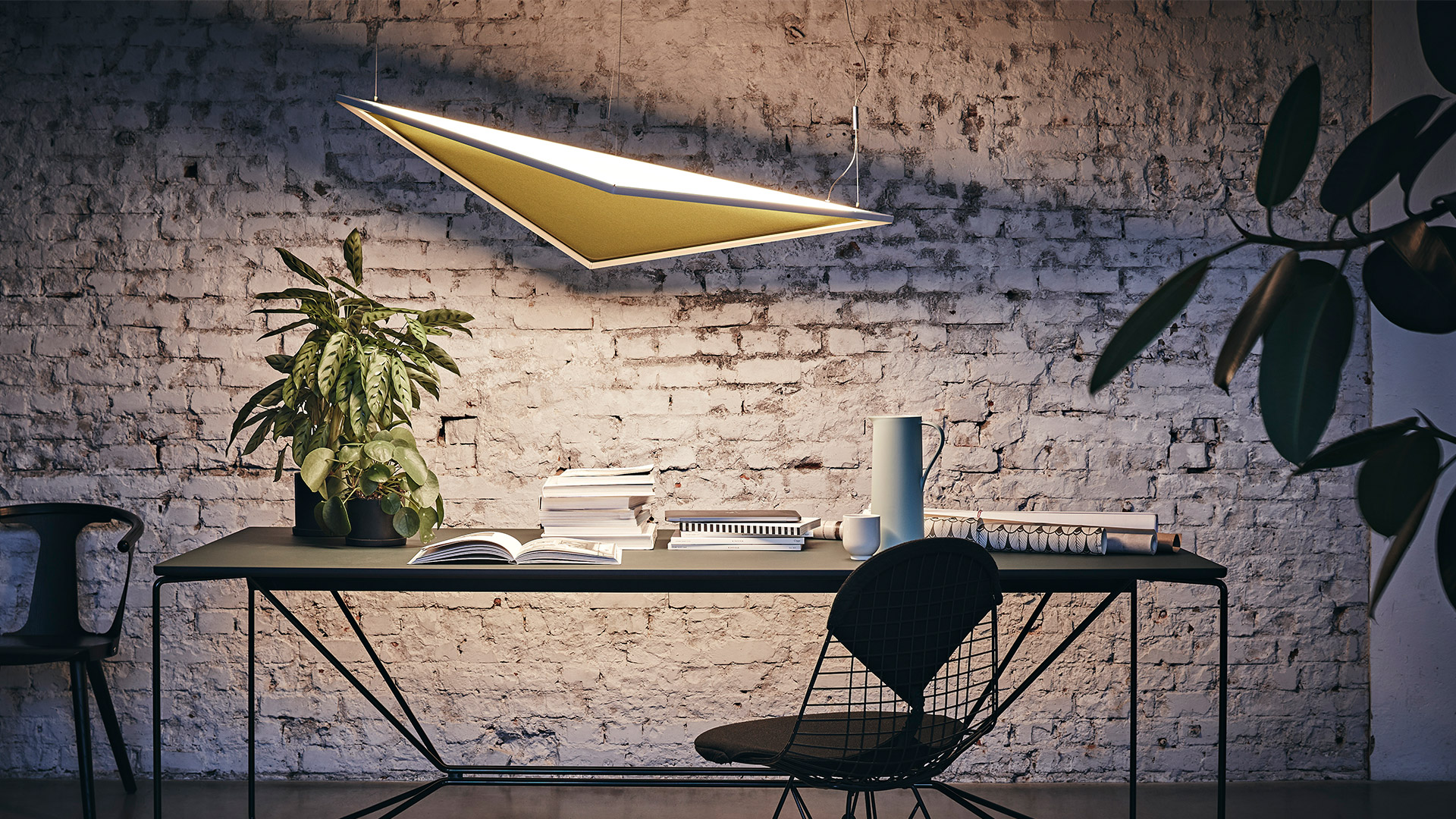Designer che regge la lampada a sospensione LED rettangolare sottile Artemide Flexia in uno studio creativo con piante e tavole di progetto