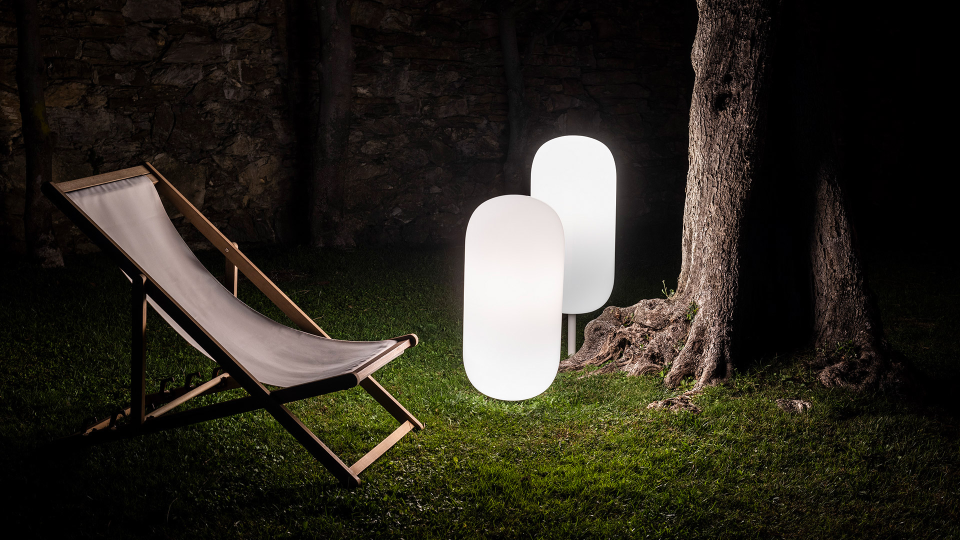 Lampada a sospensione Artemide Gople Outdoor luminosa e calda, appesa tra i rami di un pino al tramonto con luce diffusa