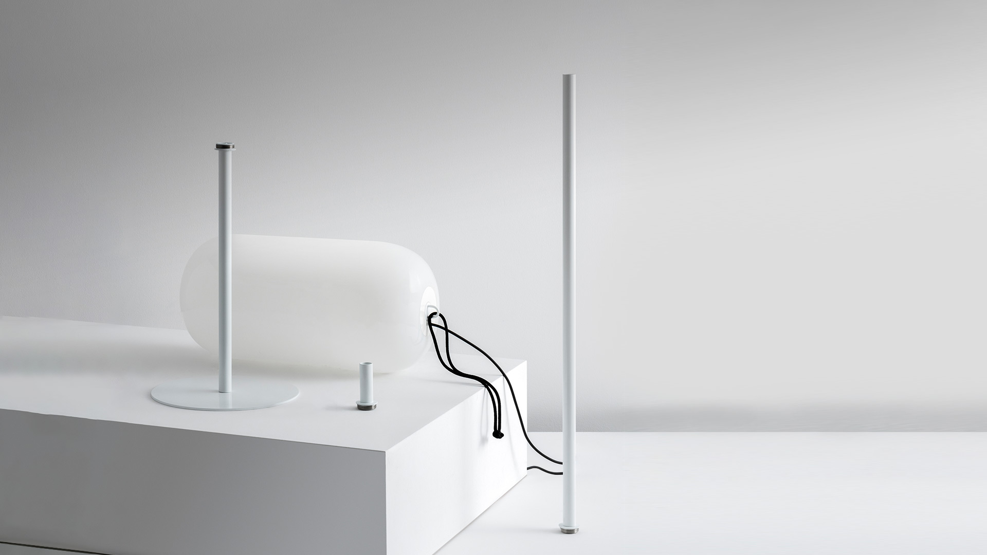 Due lampade Artemide Gople Outdoor luminose bianche su un prato di notte, accanto a una sedia a sdraio e al tronco di un albero