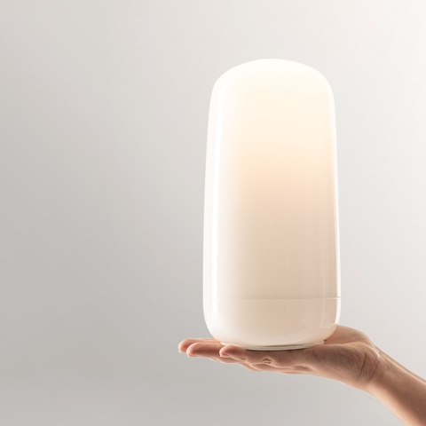 Mano che regge la lampada Artemide Gople Portable, un diffusore bianco opale compatto dalla forma arrotondata che emette luce calda