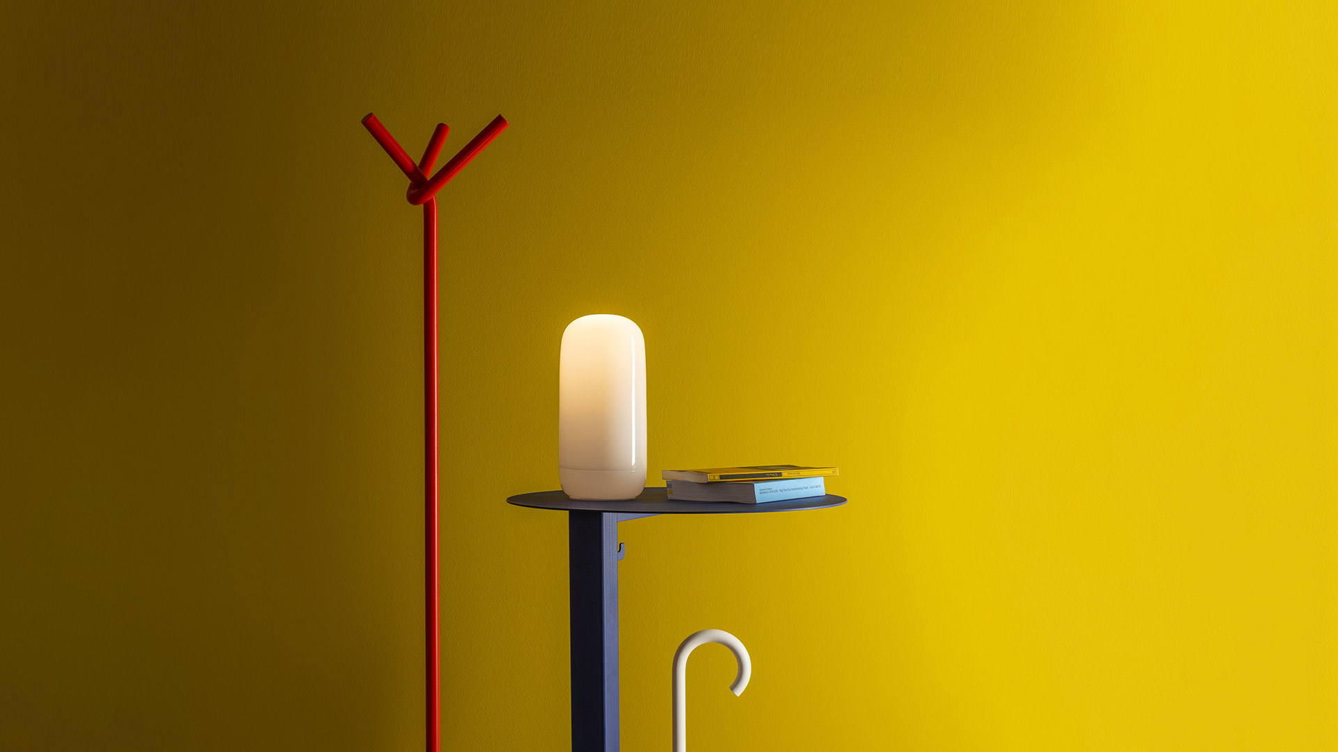 Mano che regge la lampada Artemide Gople Portable, un diffusore opalino bianco luminoso dalla forma a capsula arrotondata.