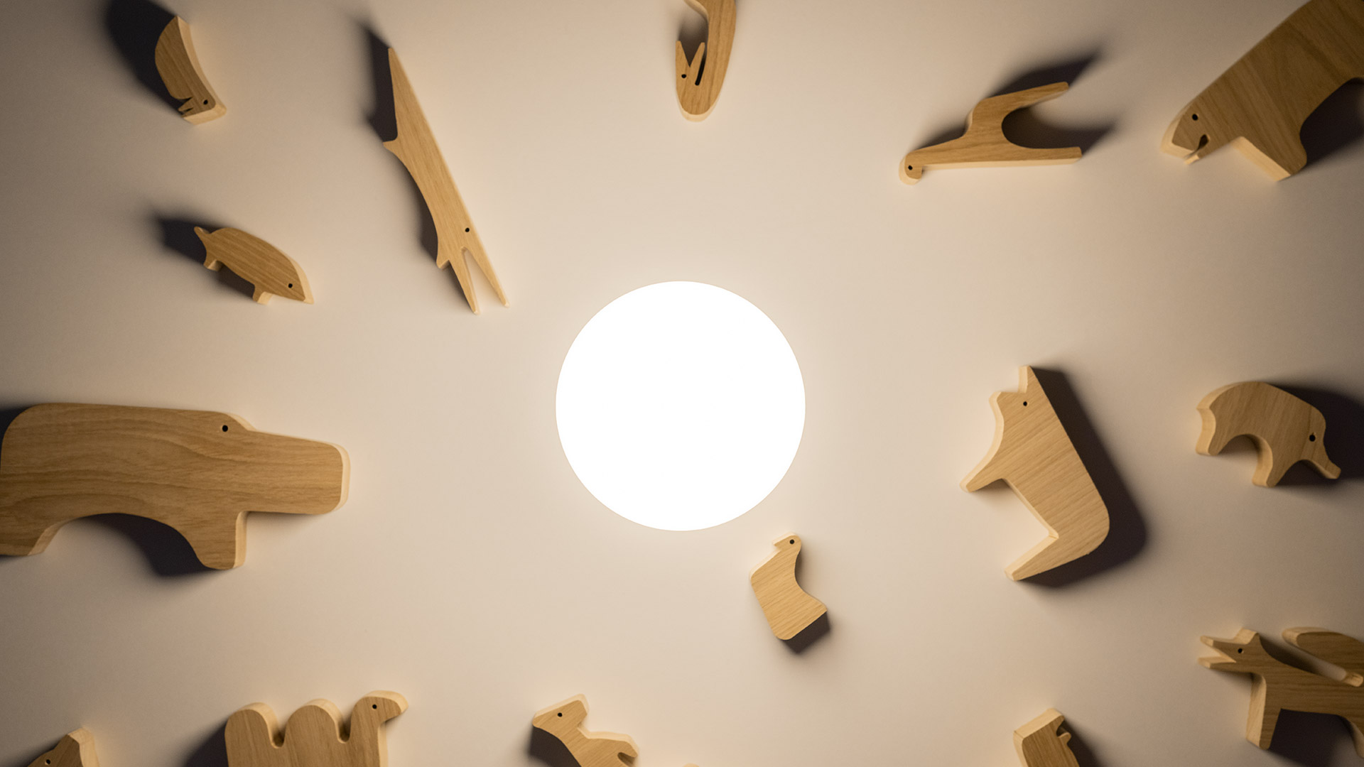Lampada Artemide Gople Portable, forma a capsula bianca luminosa, su tavolino scuro accanto ad appendiabiti rosso a Y, sfondo giallo