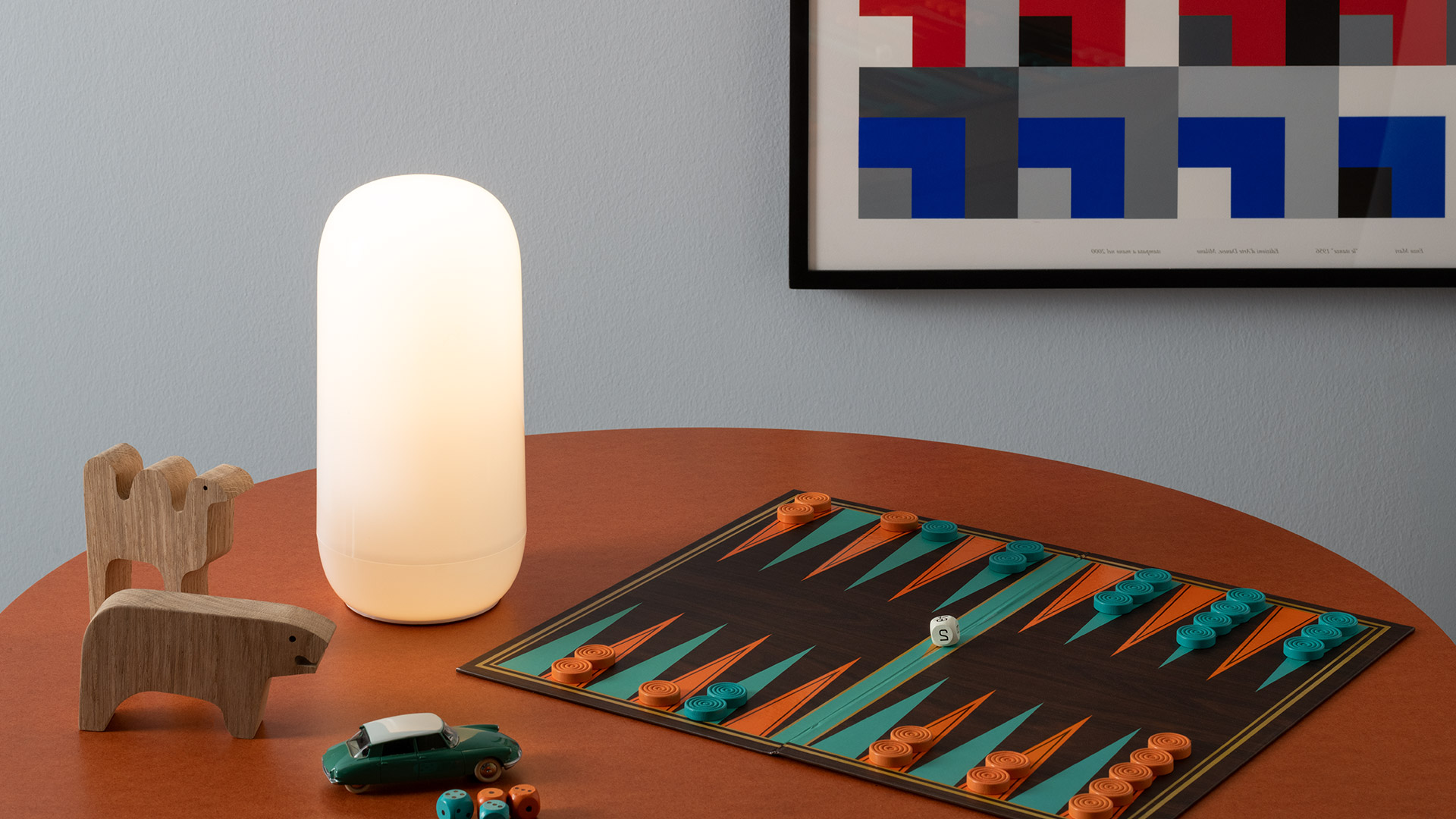 Lampada Artemide Gople Portable che illumina calorosamente all'aperto al tramonto, posata sull'erba accanto a un libro aperto e una tazza su una coperta a righe