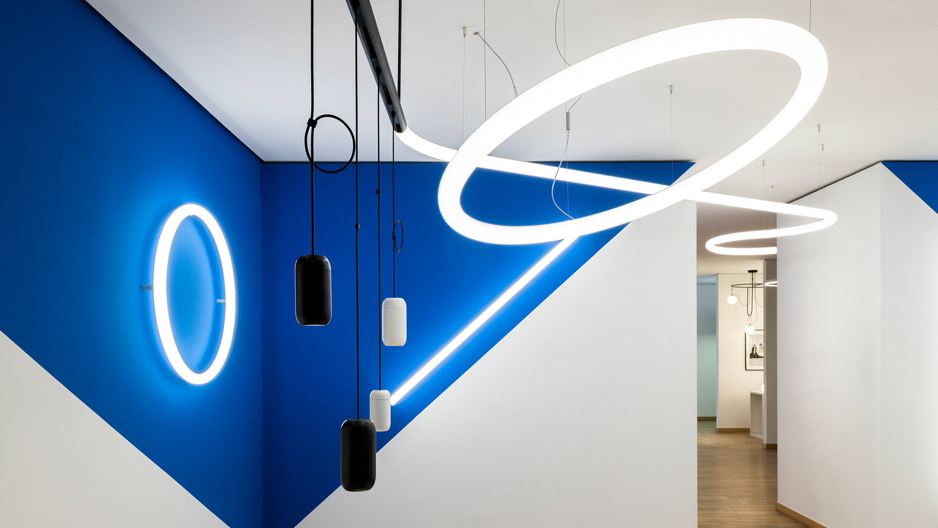 Artemide Gople System: tre faretti cilindrici bianchi su binario e due lampade a sospensione bianche a capsula appese a un binario nero