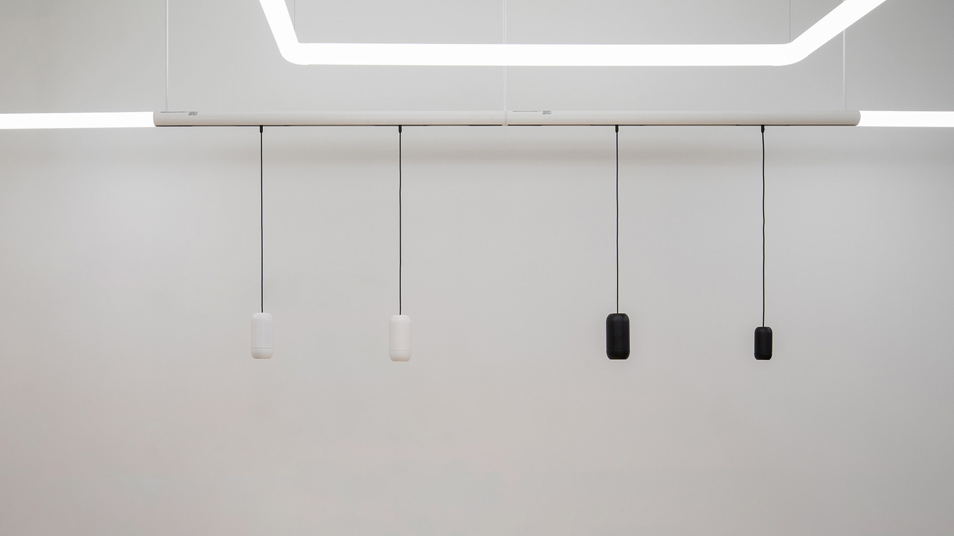 Artemide Gople System: quattro sospensioni cilindriche su binario bianco, due bianche e due nere, appese a un sistema LED geometrico a soffitto