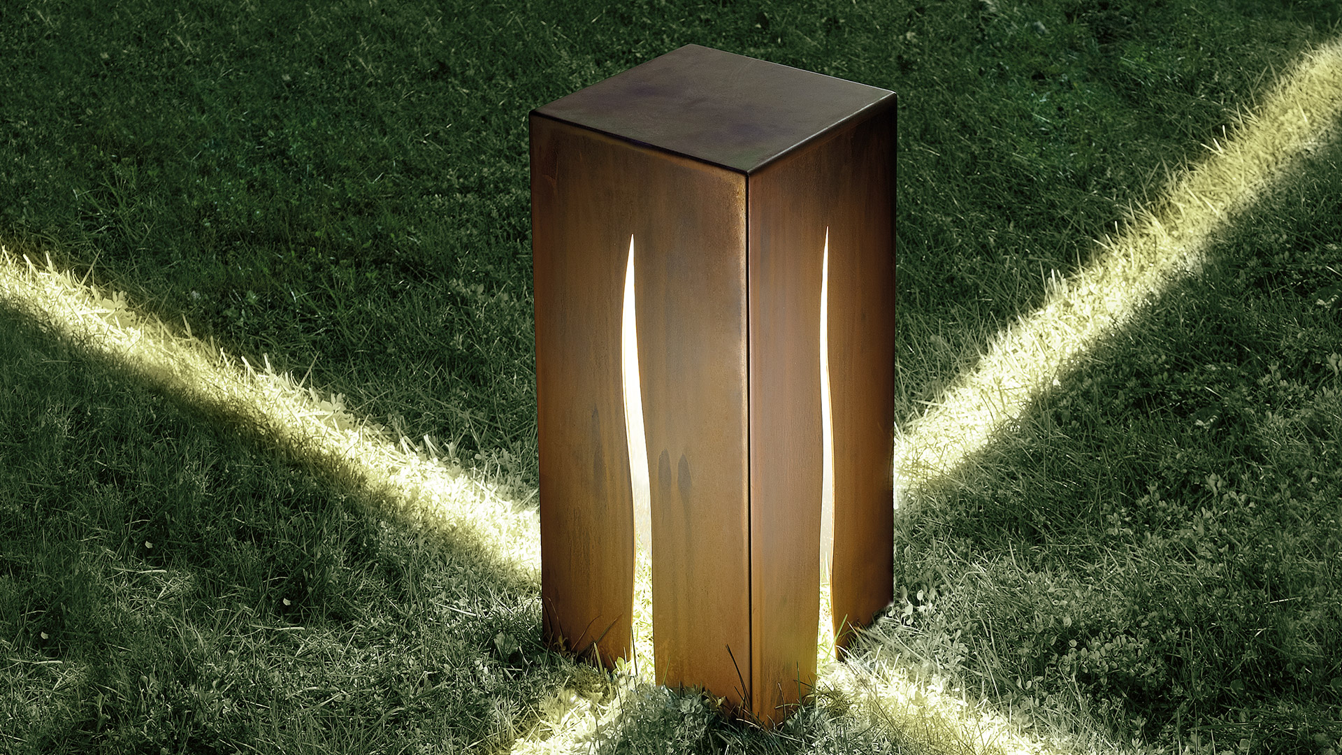 Luce da terra outdoor Artemide Granito: cubo in acciaio corten scuro con fessura verticale luminosa, su base in cemento in giardino