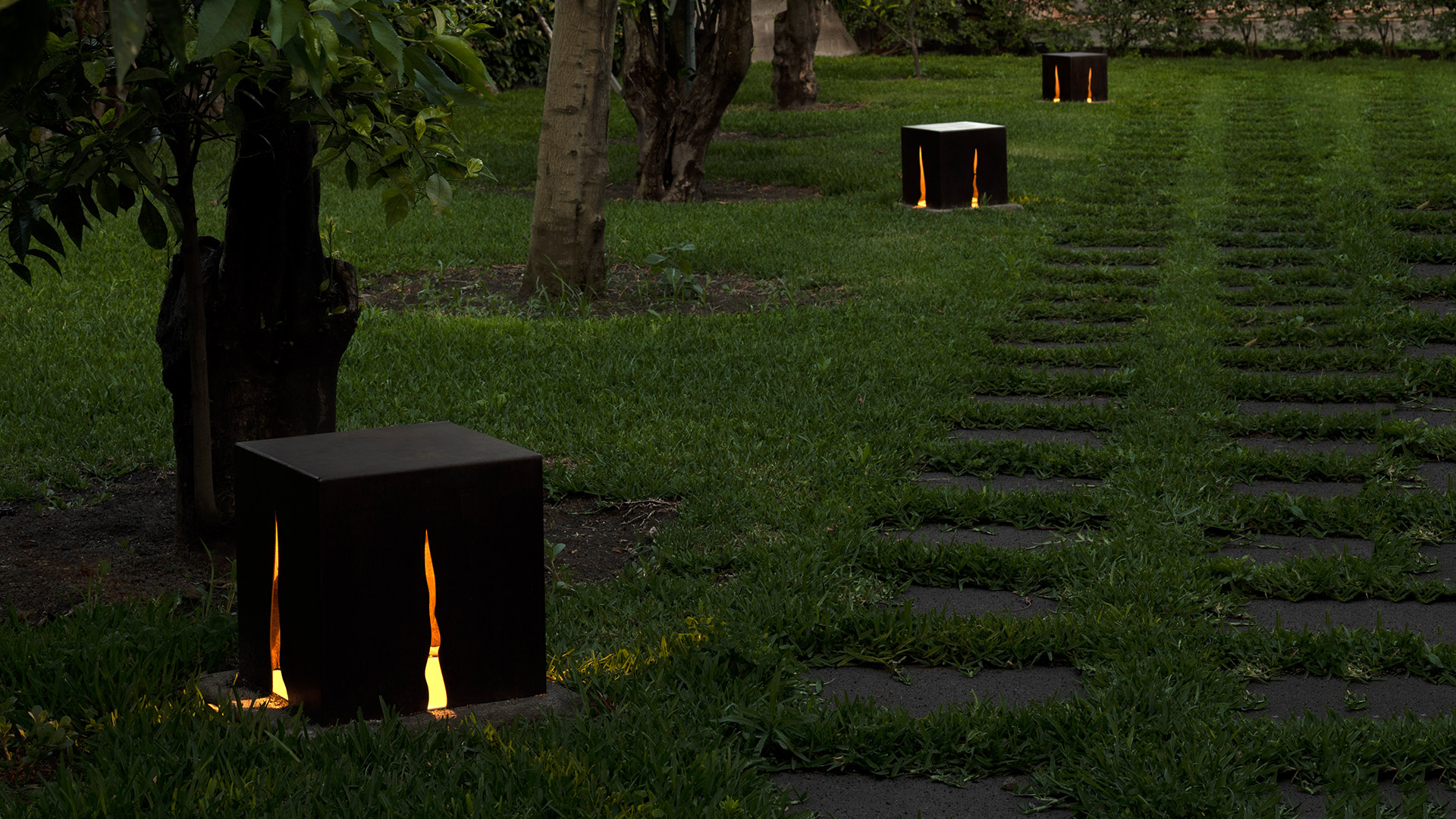 Lampada da esterno Artemide Granito in acciaio Corten, con luce calda che fuoriesce da fessure verticali sull'erba circostante