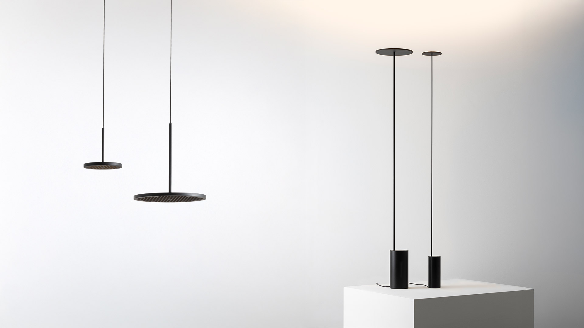 Primo piano della sommità della lampada da terra Artemide Helgoland: paralume a disco circolare piatto nero che emette luce calda su un sottile stelo nero