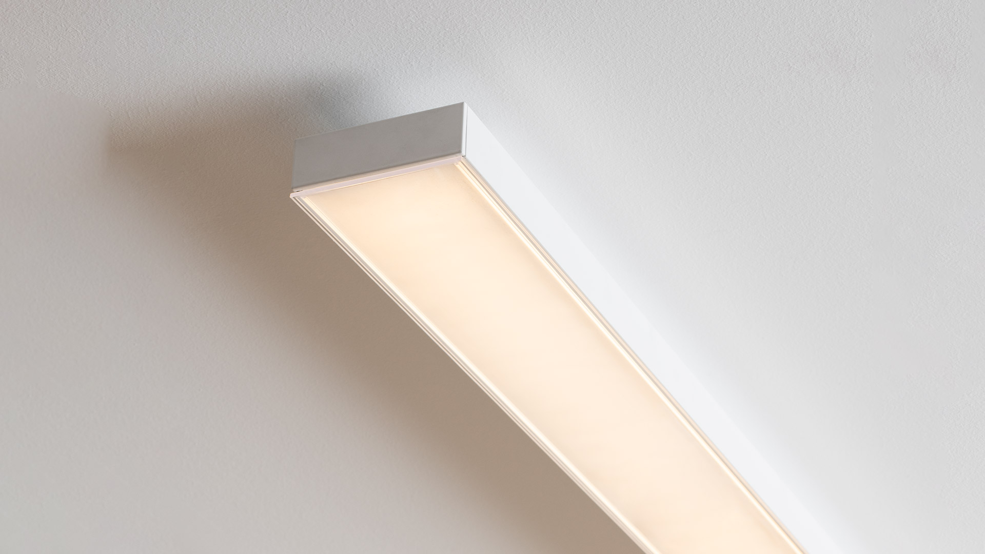 Two Artemide Hoy Linear Stand Alone pendant lamps: upper white aluminum profile, lower dark gray, both emitting warm diffused LED light