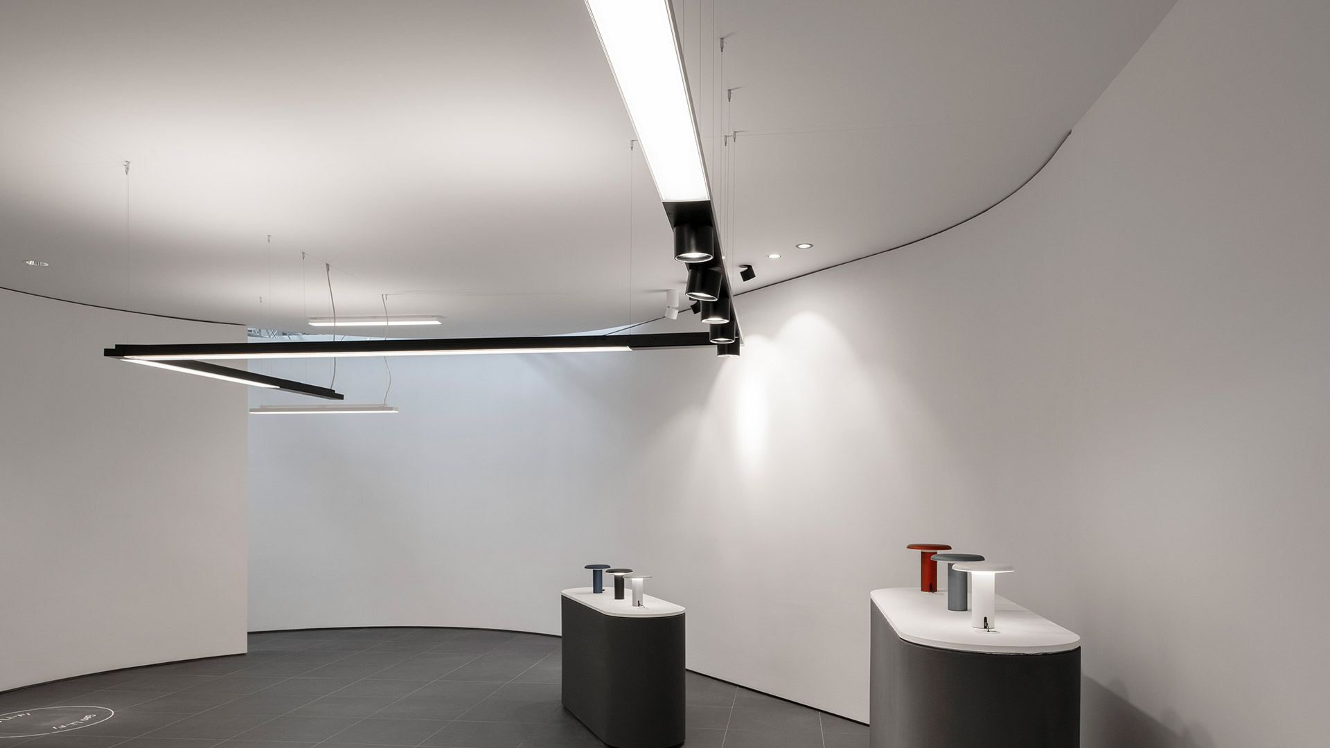 Artemide Hoy System: telaio rettangolare a soffitto che combina una striscia LED lineare e faretti direzionali regolabili su struttura in metallo scuro