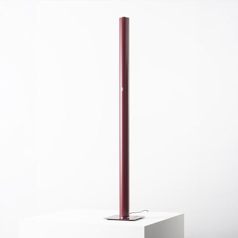 Lampada da terra Artemide Ilio: sottile colonna LED cilindrica bordeaux su base quadrata piatta, emette luce ambientale indiretta