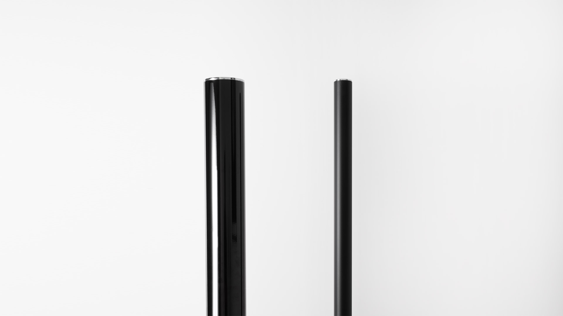 Three Artemide Ilio floor lamps in red, white, and black, featuring slim cylindrical columns on square bases in a minimalist white room