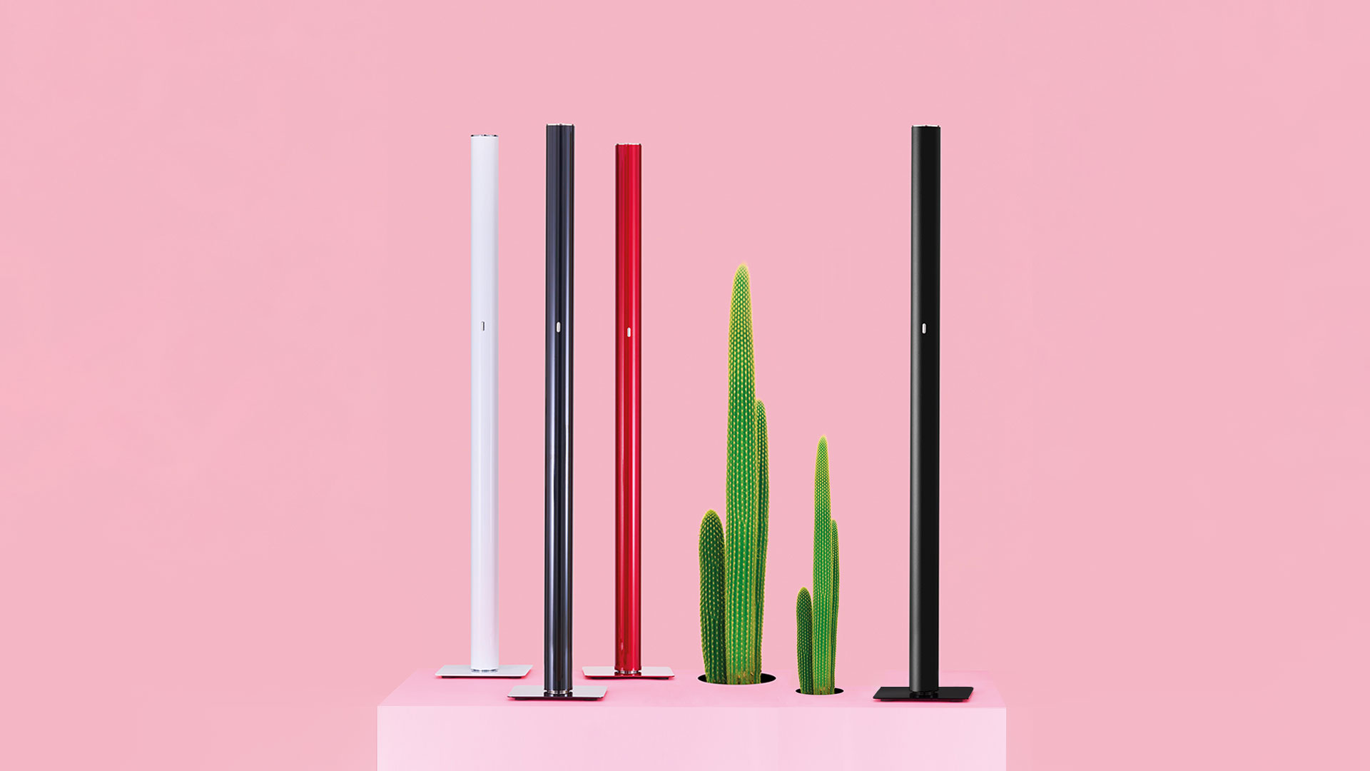 Tre lampade da terra Artemide Ilio in rosso, bianco e nero, con colonne cilindriche sottili su basi quadrate in una stanza minimalista bianca