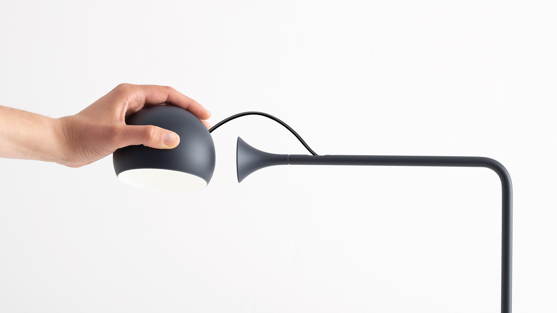 Lampada da terra Artemide Ixa con braccio regolabile in finitura nera accanto a un divano in pelle marrone su parete di mattoni bianchi