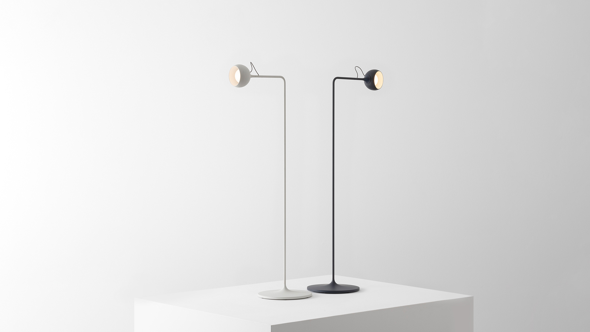Cucina moderna con tre lampade a sospensione Artemide Ixa nere sopra un'isola, luce calda, pavimento a spina di pesce, grande finestra al crepuscolo