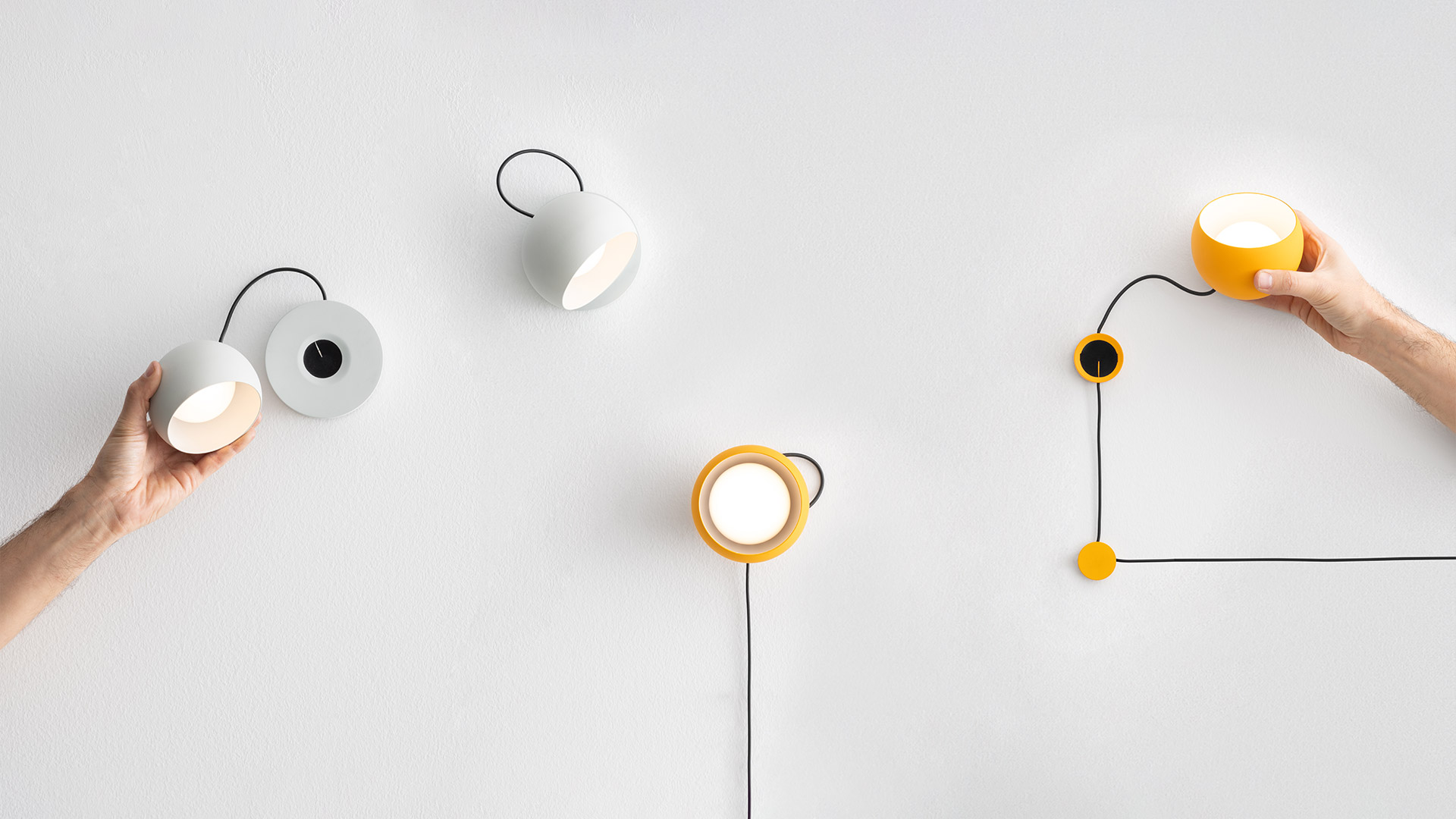 Due lampade da parete Artemide Ixa: sinistra paralume a cupola bianco con gancio nero, destra paralume ad anello giallo con cavo nero e sfera dimmer gialla