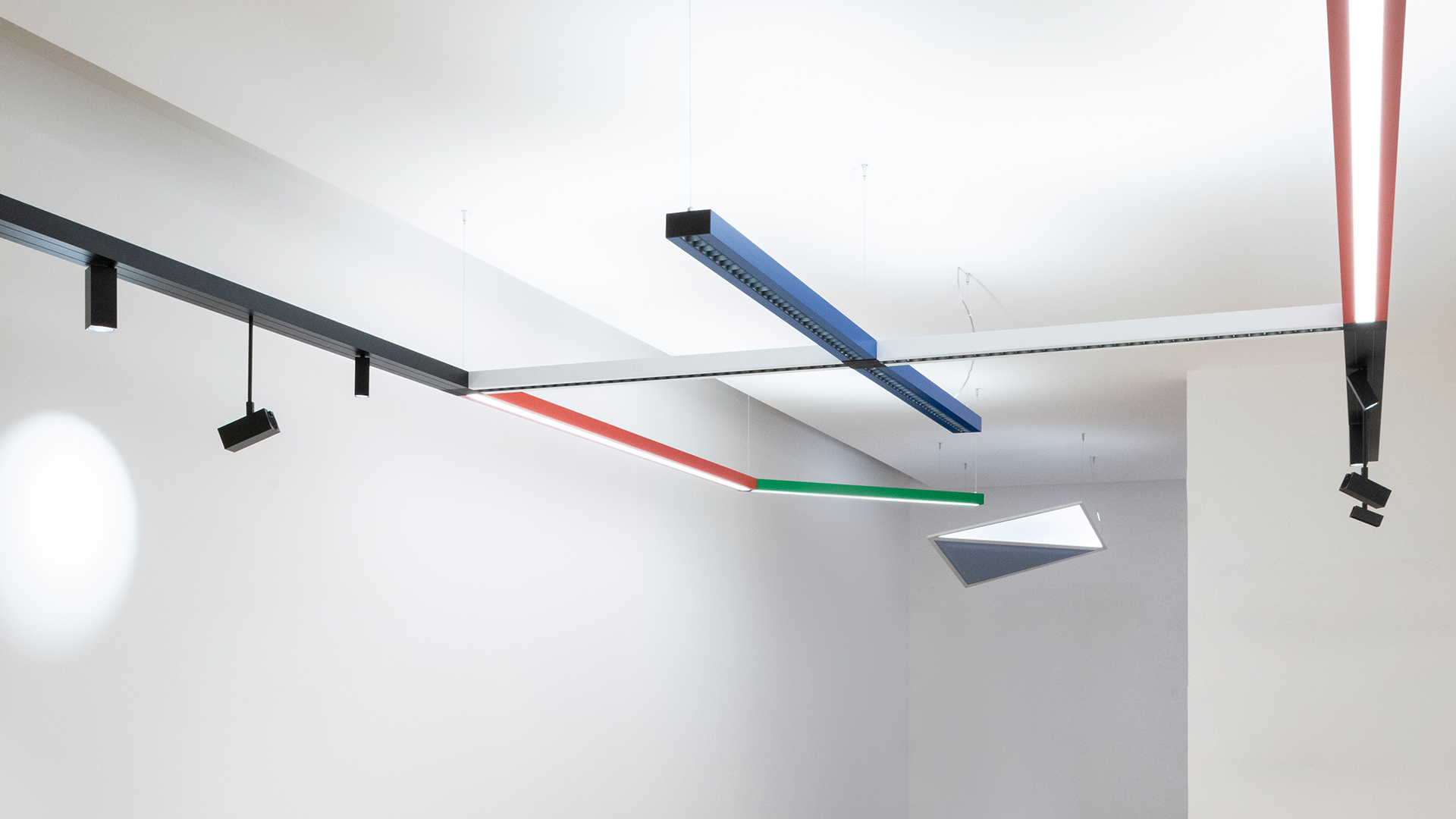 Sistema di illuminazione a soffitto modulare Artemide Katà Métron con profili lineari colorati in blu, verde, rosso e nero con faretti orientabili.