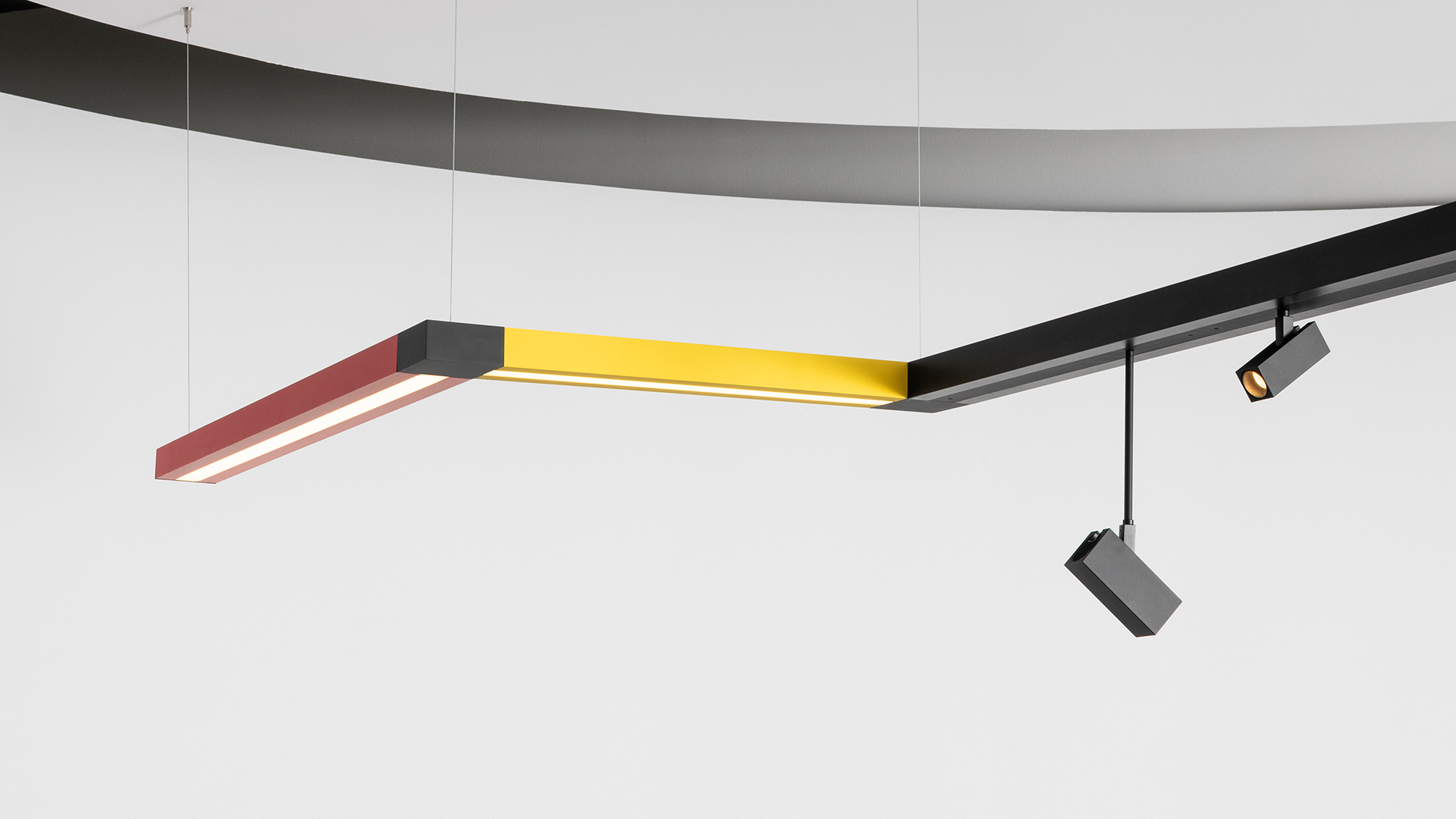 Installazione a soffitto Artemide Katà Métron con faretti su binario nero, elementi LED lineari colorati in rosso, verde, blu e pannello bianco