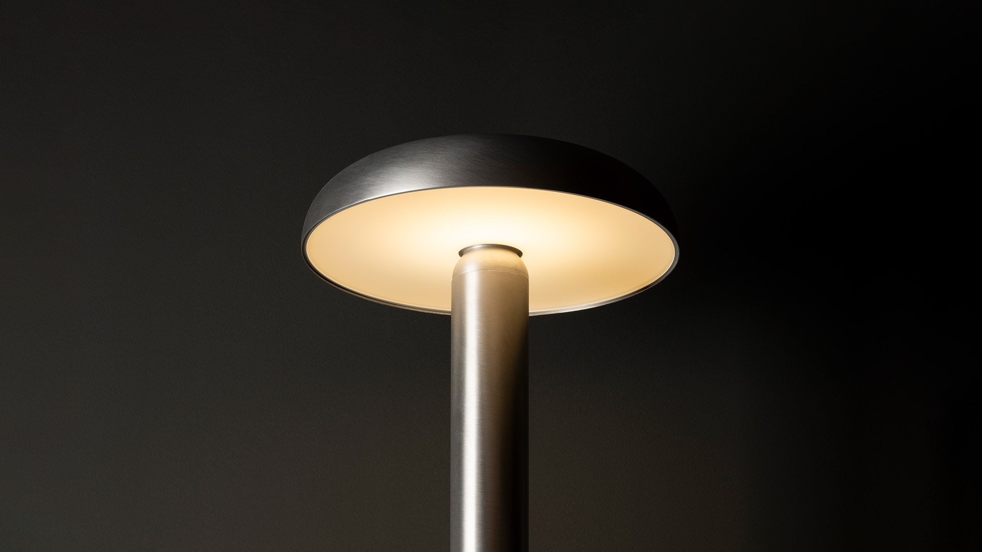 Lampada da tavolo Artemide Knop: sottile stelo dorato sormontato da un ampio paralume a disco piatto in metallo scuro con luce calda diffusa