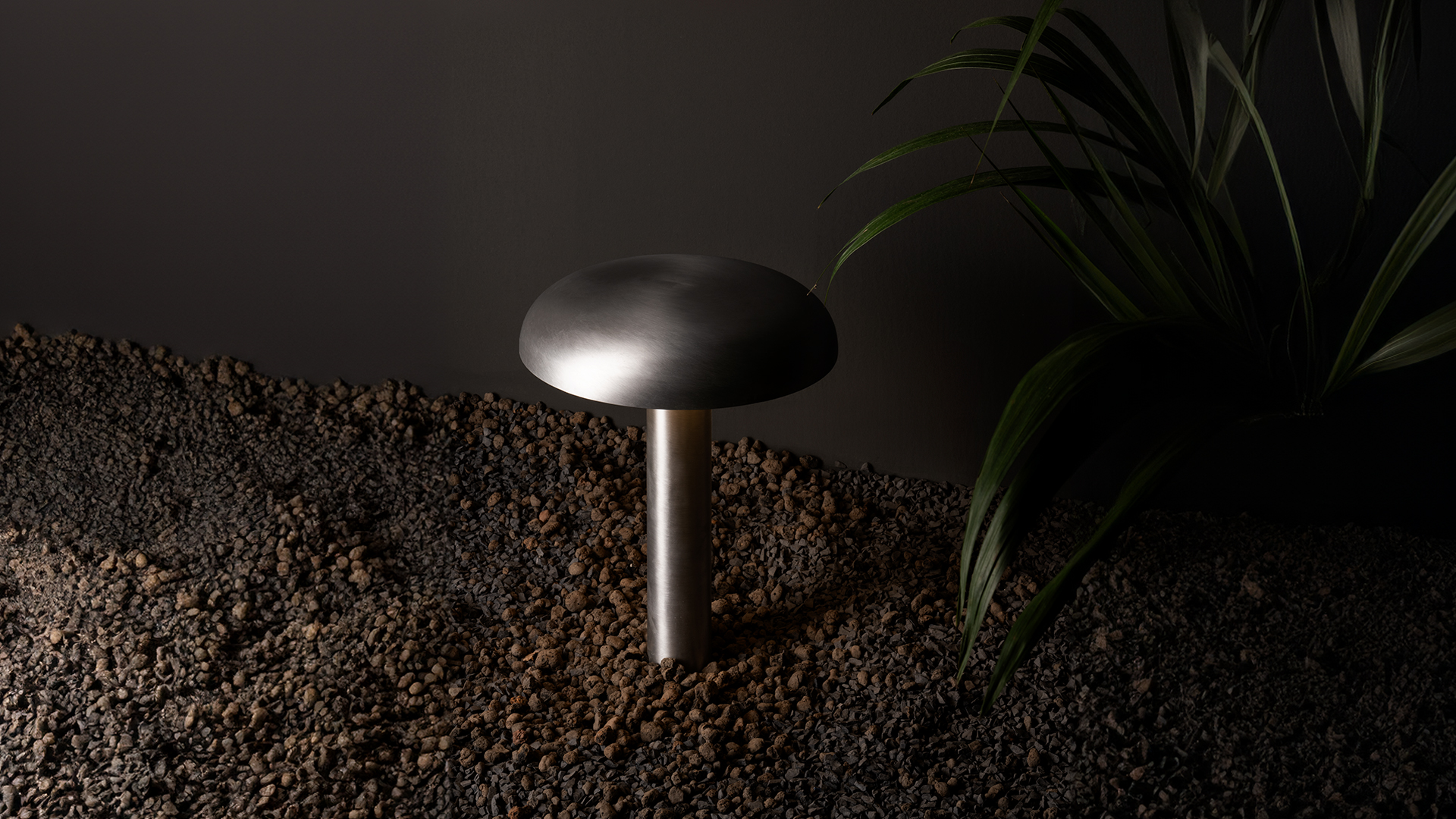 Donna in un giardino con paletti e lampade da esterno Artemide Knop tra piante rigogliose e fiori su un'isola di erba