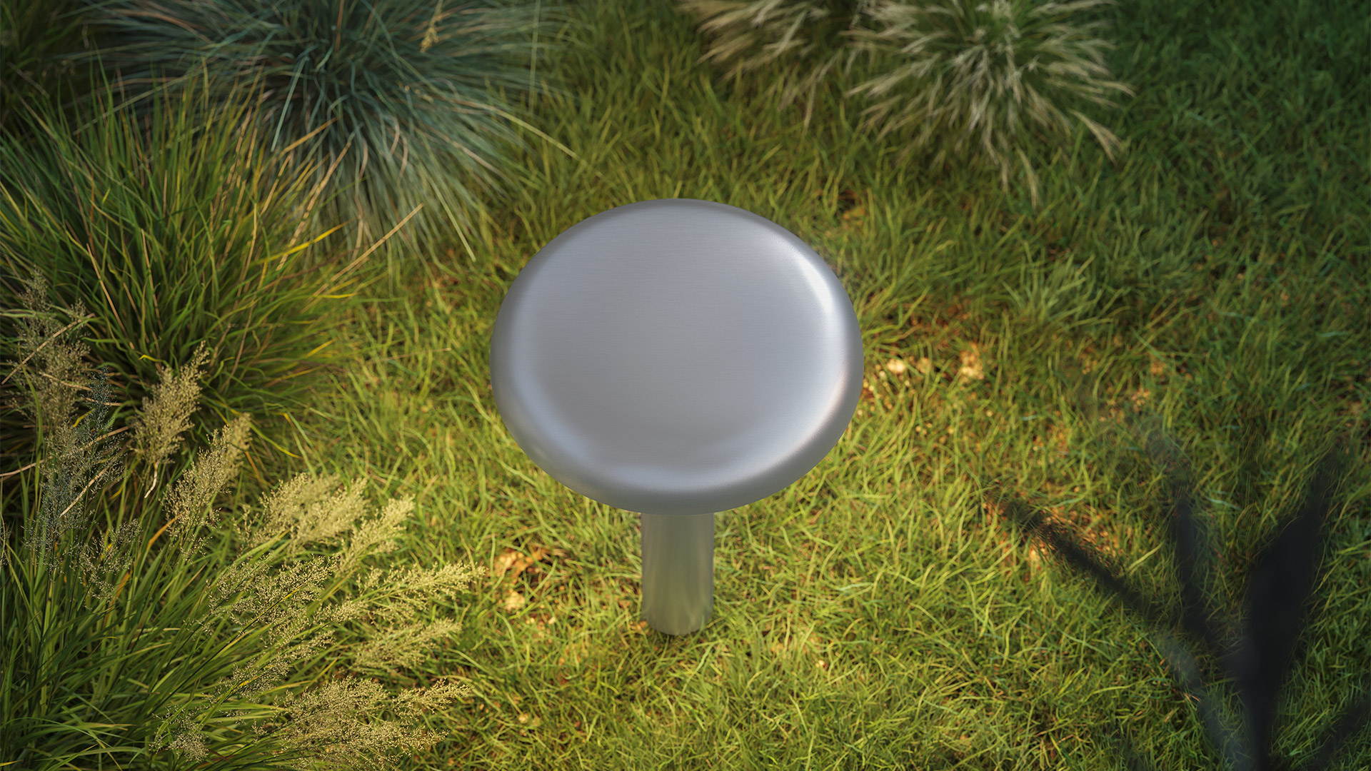 Lampada da esterno Artemide Knop: apparecchio a forma di fungo con paralume a disco scuro su sottile stelo, posizionata tra ghiaia scura vicino a pianta tropicale