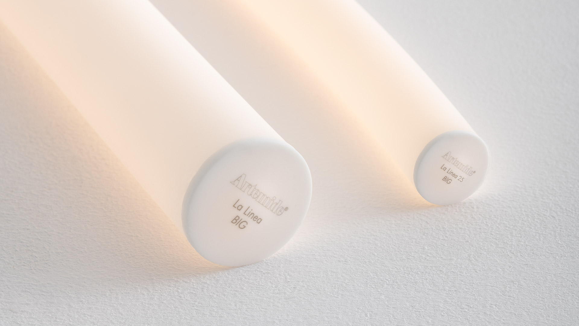 Lampada a soffitto LED sinuosa Artemide La Linea sopra un tavolo da pranzo in legno, su parete scura con due stampe pop-art di frutta